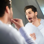 man looking at his mouth in the mirror