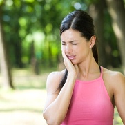 woman outside holding her cheek in pain