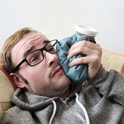 man lying on a couch and holding an ice pack to his cheek