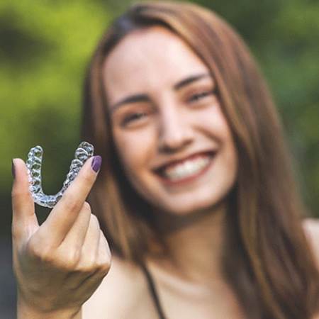 Patient using Invisalign in Fresno smiling while holding up aligner