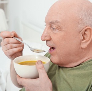 An elderly man who’s eating soup in bed