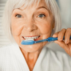 An elderly lady brushing her teeth after dental implant placement
