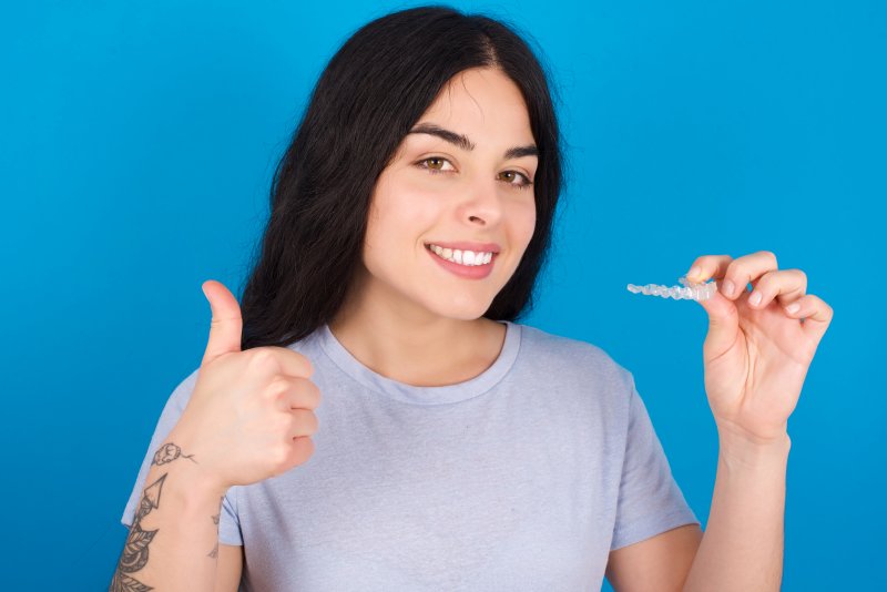 person holding Invisalign, giving thumbs-up, and smiling