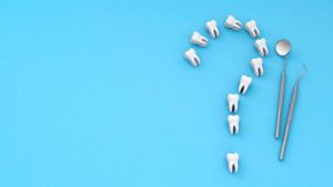 Model teeth forming the shape of a question mark next to dental instruments on a blue background