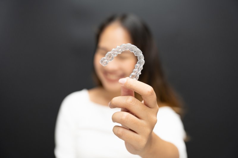 A woman smiling as she holds up her Invisalign aligner